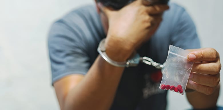 Man wearing handcuffs holding baggie of red pills